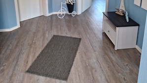 Ein Flur mit Holzboden, einem kleinen Teppich, einem weißen Fahrrad und einer Kommode mit Spiegel.