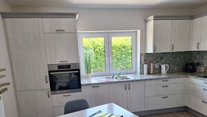 Eine moderne Küche mit weißen Schränken, einem Einbauofen, einer Spüle und einem Fenster mit Blick ins Grüne.