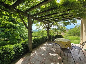 A covered patio with a table and chairs, surrounded by lush greenery and a view of the countryside. - Pech Ferrat, Pleine Campagne sur 1 Ha Arboré, vue sur la Vallée et les Coteaux (Saint-Amans-du-Pech)