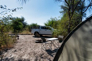 A white pickup truck parked in a campsite with a tent and camping chairs set up nearby.