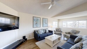 A living room with a dark blue sofa, a white coffee table, and patterned armchairs. There are two framed wall art pieces above the sofa.