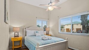 A bedroom with a bed, two bedside tables with lamps, a ceiling fan, and a window with blinds.