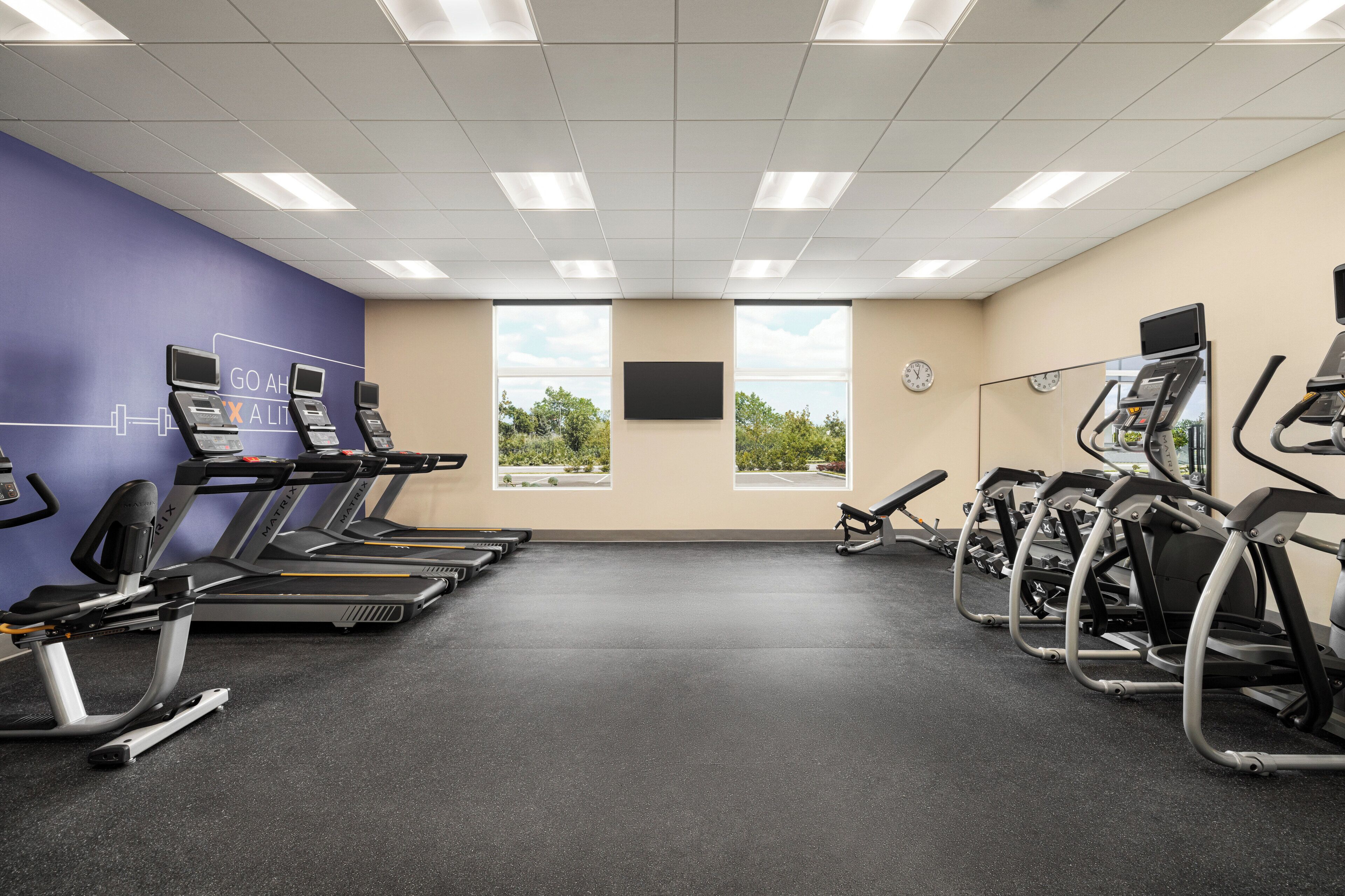 Un gimnasio con cintas de correr, elípticas y bicicletas estáticas dispuestas en filas.