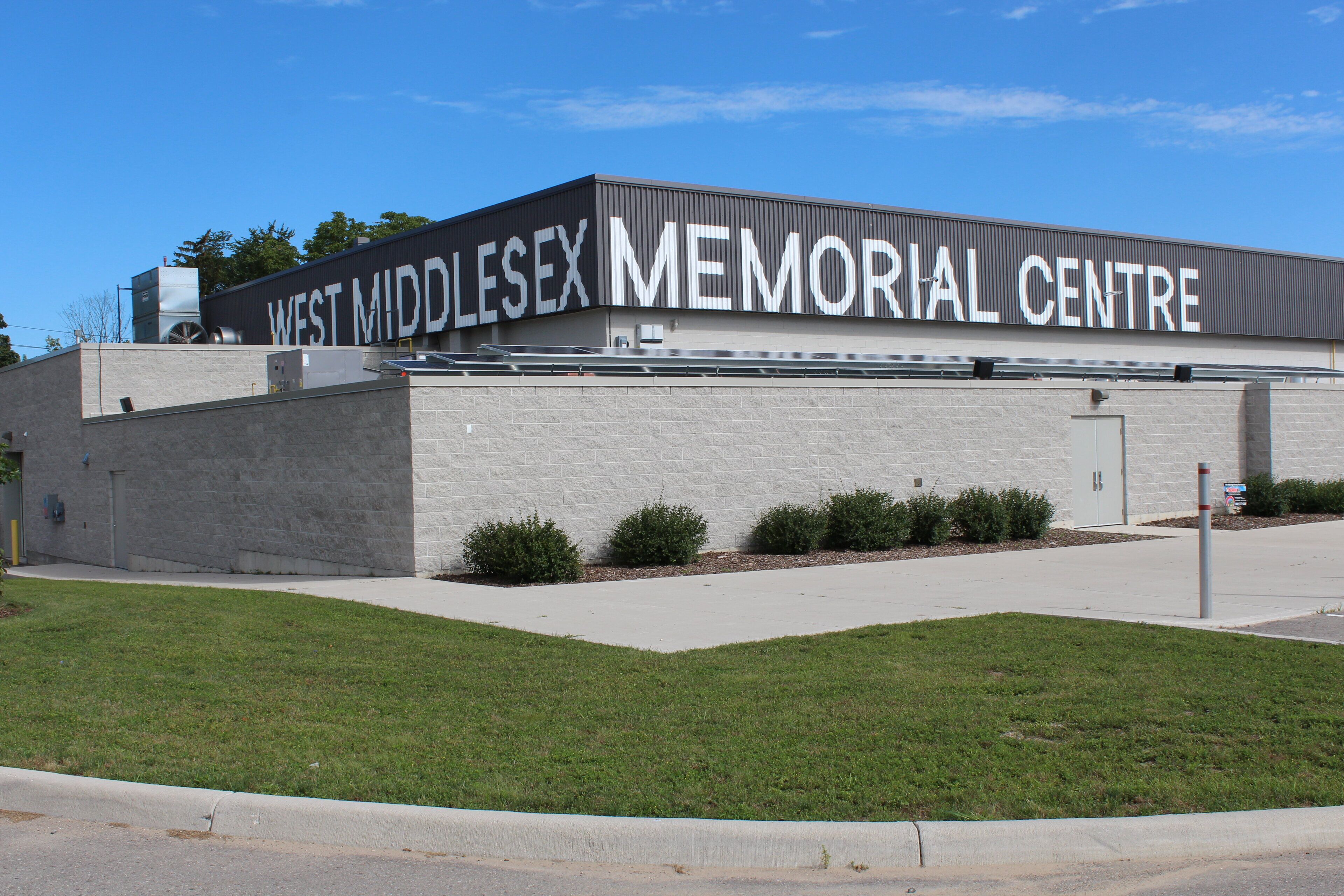 The exterior of the West Middlesex Memorial Centre, featuring a modern building with a flat roof, large windows, and a landscaped front yard with small bushes.