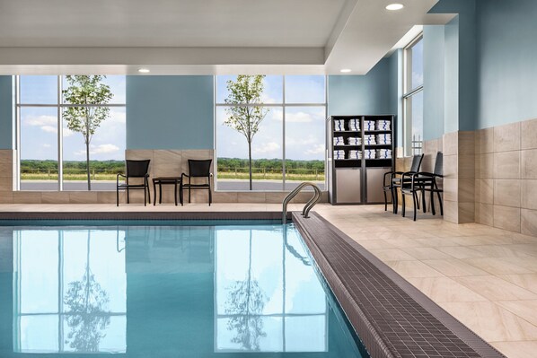 A modern indoor pool with clear views of the outdoors, including trees and a distant landscape.