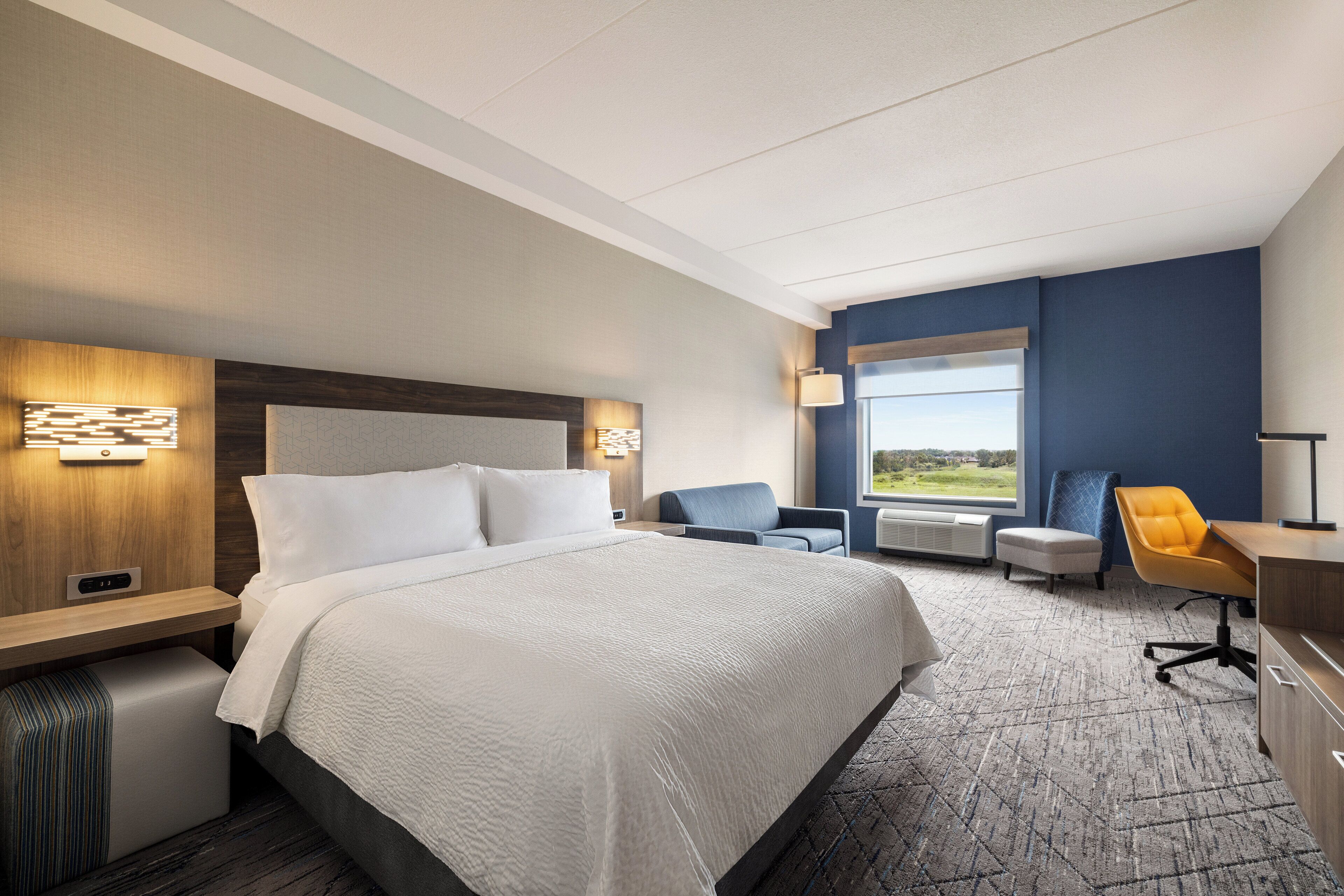 A hotel room with a large bed, a desk, a chair, and a window with a view.