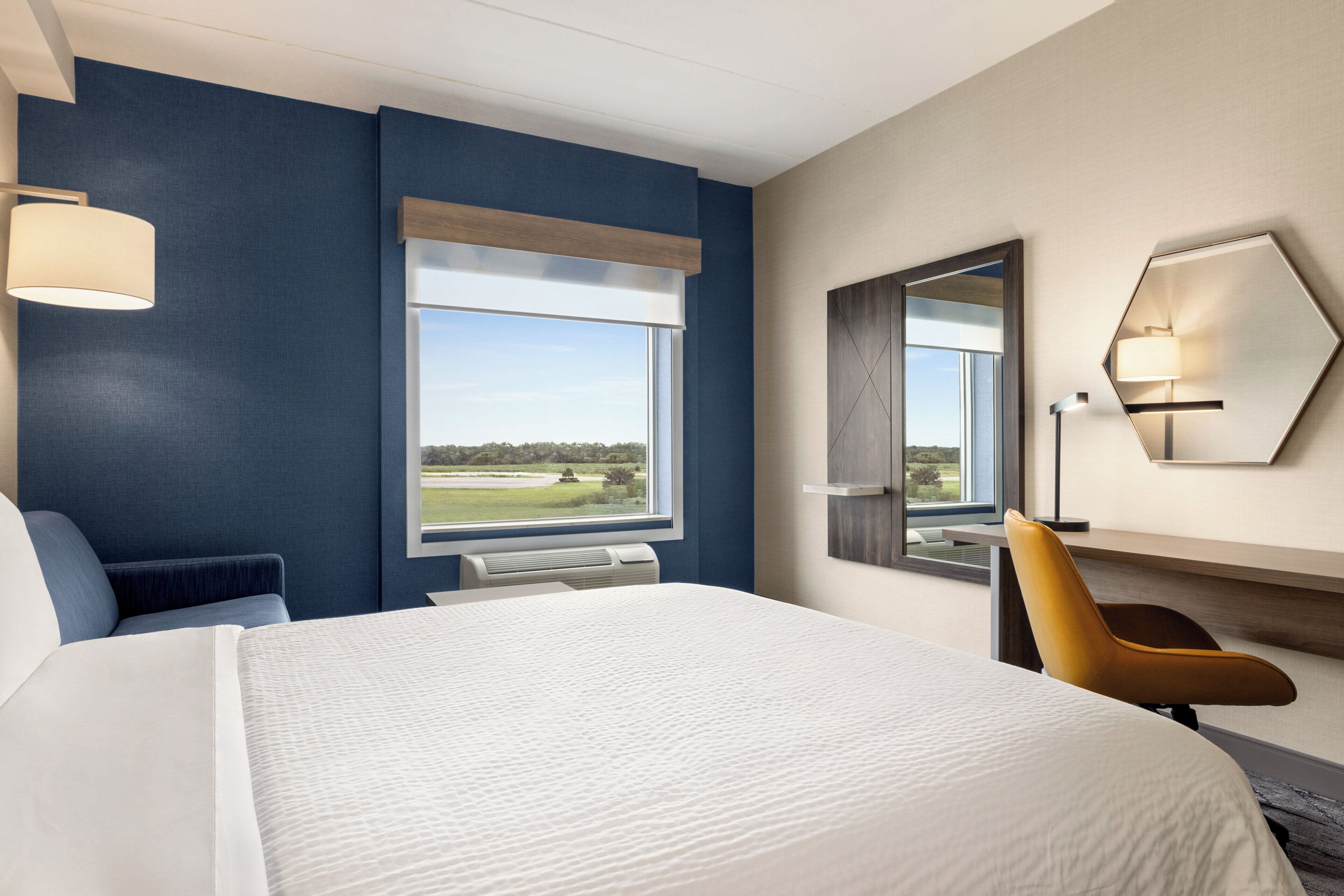 A hotel room with a large bed, a desk, a chair, a window with a view of a landscape, and a mirror on the wall.