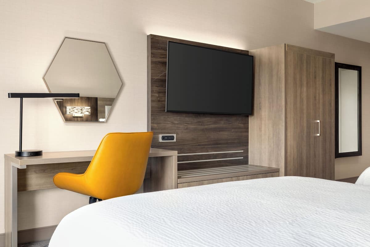 Une chambre d’hôtel comprenant un lit, un bureau avec une chaise, un téléviseur à écran plat et une armoire.