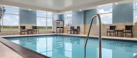 Une piscine à l’eau d’un bleu cristallin, entourée de chaises et d’une bibliothèque.