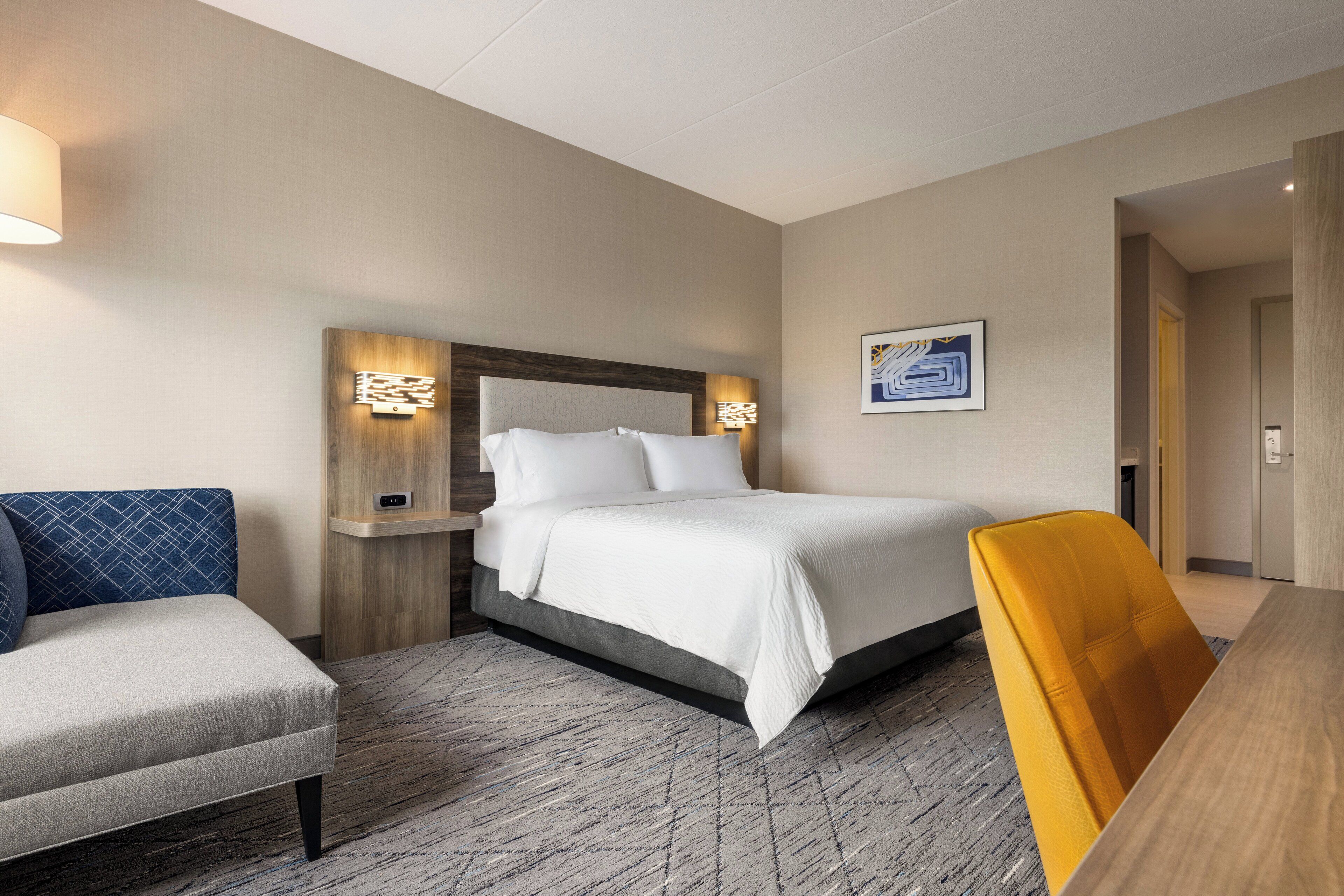 Una habitación de hotel con cama, escritorio, silla y lámpara de pared.