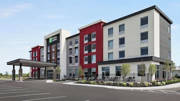 A multi-story hotel with a modern design, featuring a mix of red and neutral colors, a covered entrance, and a landscaped outdoor area with a fence and seating.