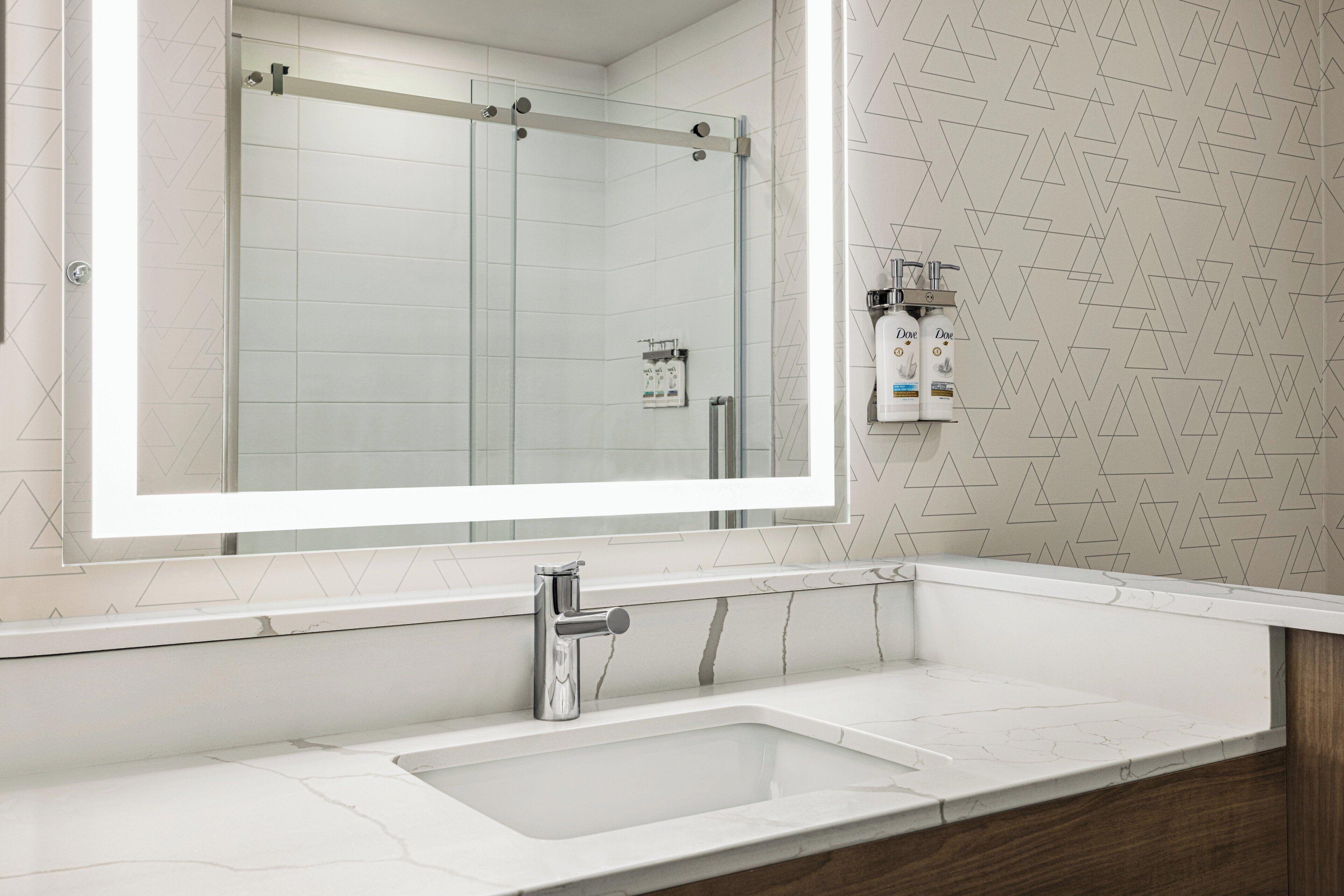 A bathroom with a large mirror, a sink, and a shower.