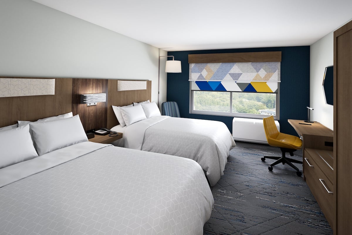 Une chambre d’hôtel avec deux lits, un bureau, une chaise, une table de chevet et une fenêtre donnant sur un paysage agréable.