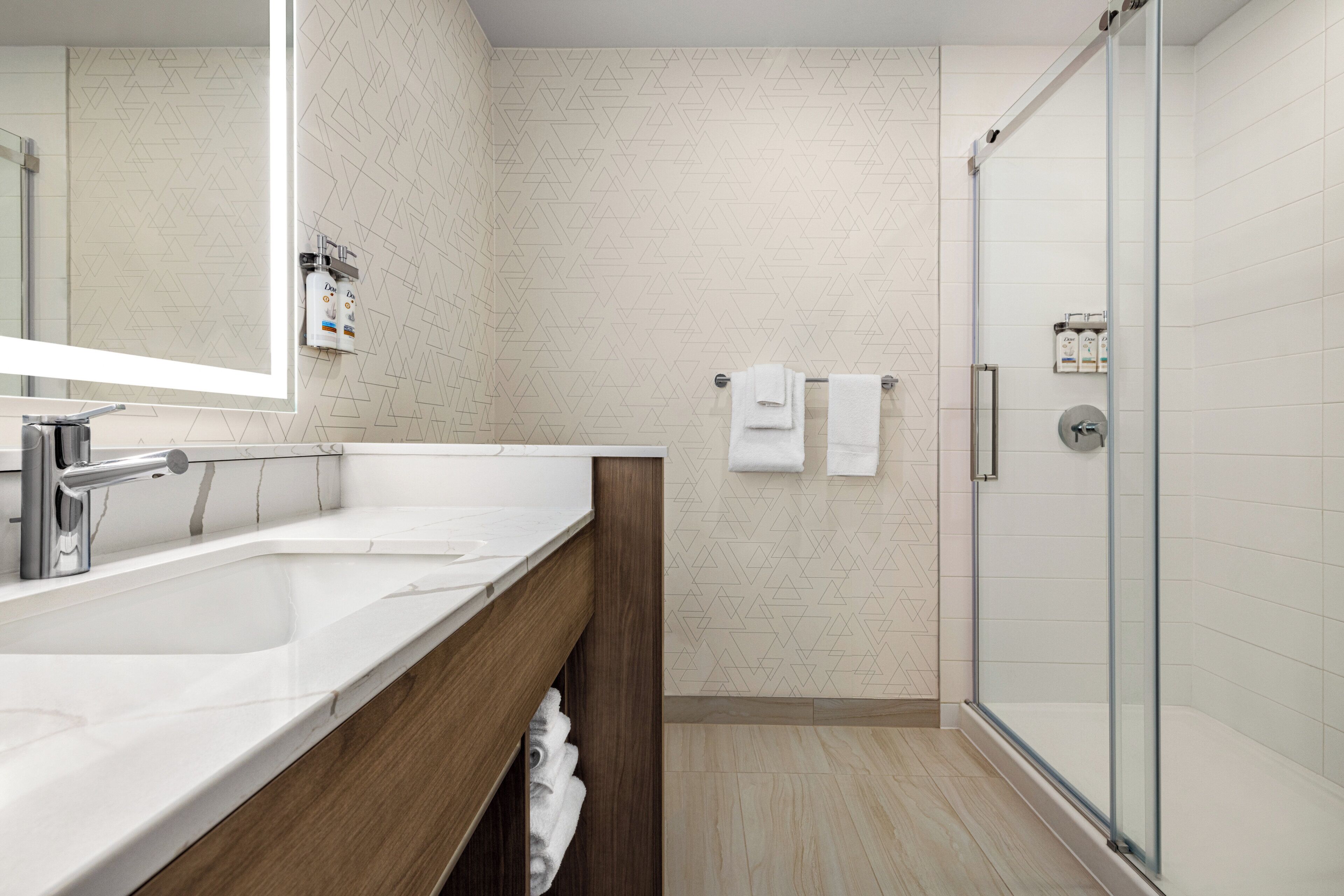Un baño moderno con cabina de ducha de vidrio, lavamanos doble y toallero.