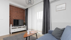 Una sala de estar moderna con una pared de ladrillo decorativa, un televisor de pantalla plana sobre un mueble blanco, un sofá gris con cojines de lunares y una mesa de centro de madera.