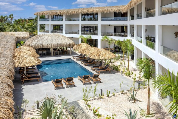 A resort with a pool, lounge chairs, and thatched umbrellas. - Belnem House Bonaire (Kralendijk)