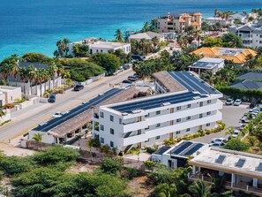 A coastal hotel with multiple buildings, solar panels on rooftops, and a view of the sea.