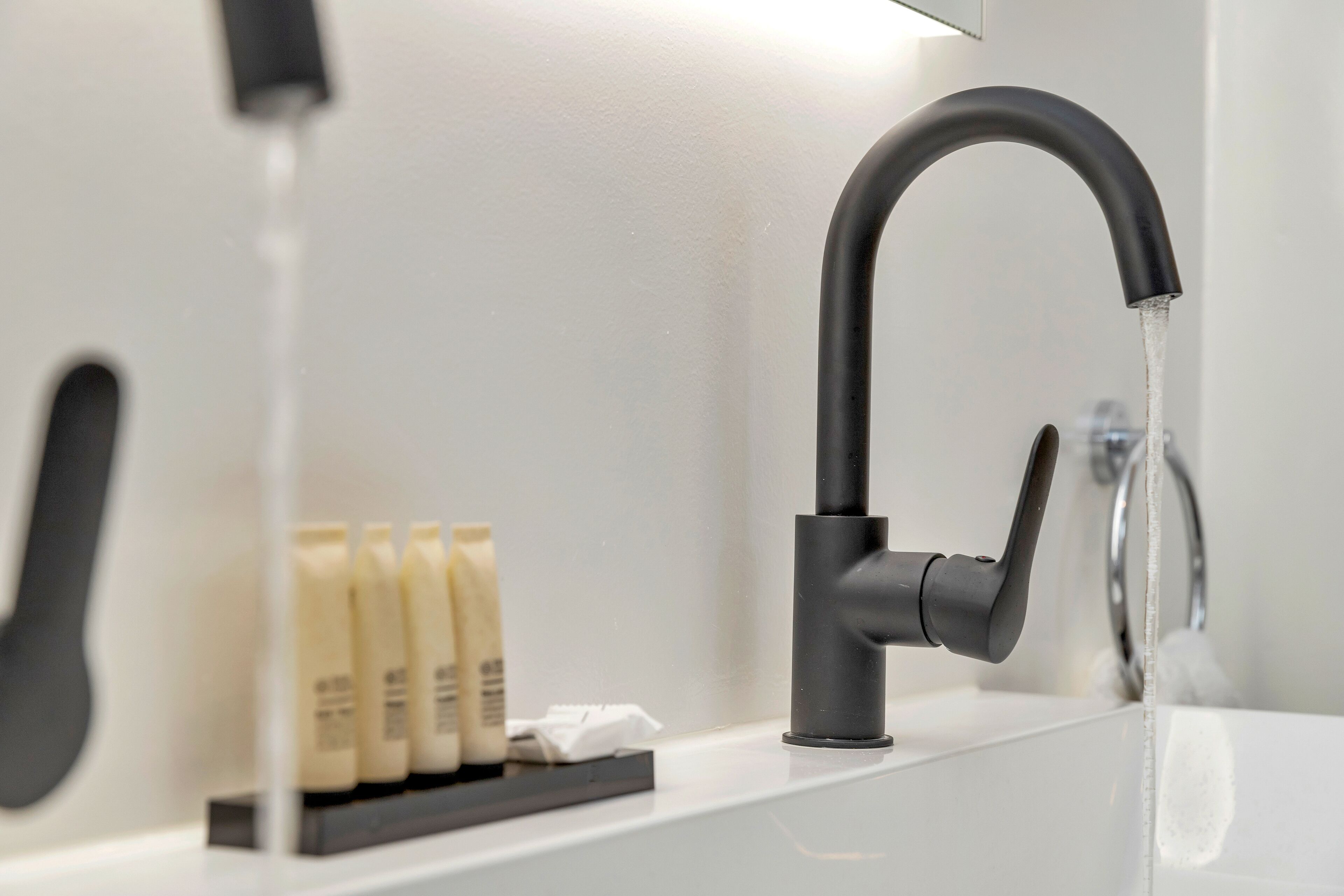 A modern bathroom with a sleek black faucet, a white sink, and a row of toiletries.