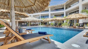 A poolside area with sun loungers, thatched umbrellas, and a clear blue pool. - Belnem House Bonaire (Kralendijk)