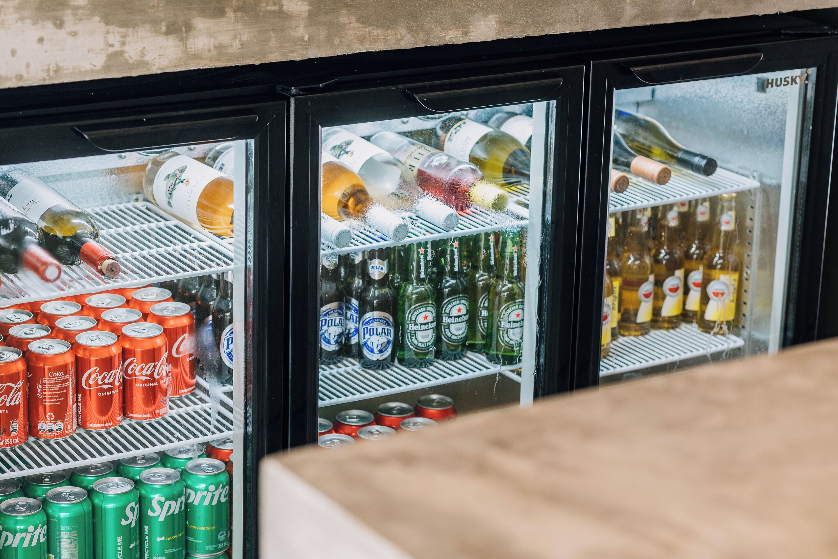 A refrigerator stocked with various beverages including soda cans, beer bottles, and wine bottles.
