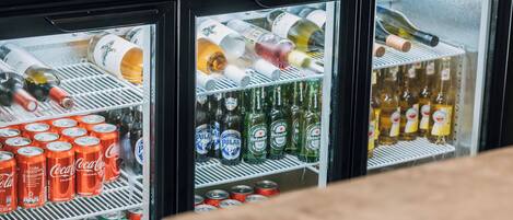 A refrigerator stocked with various beverages including soda cans, beer bottles, and wine bottles.