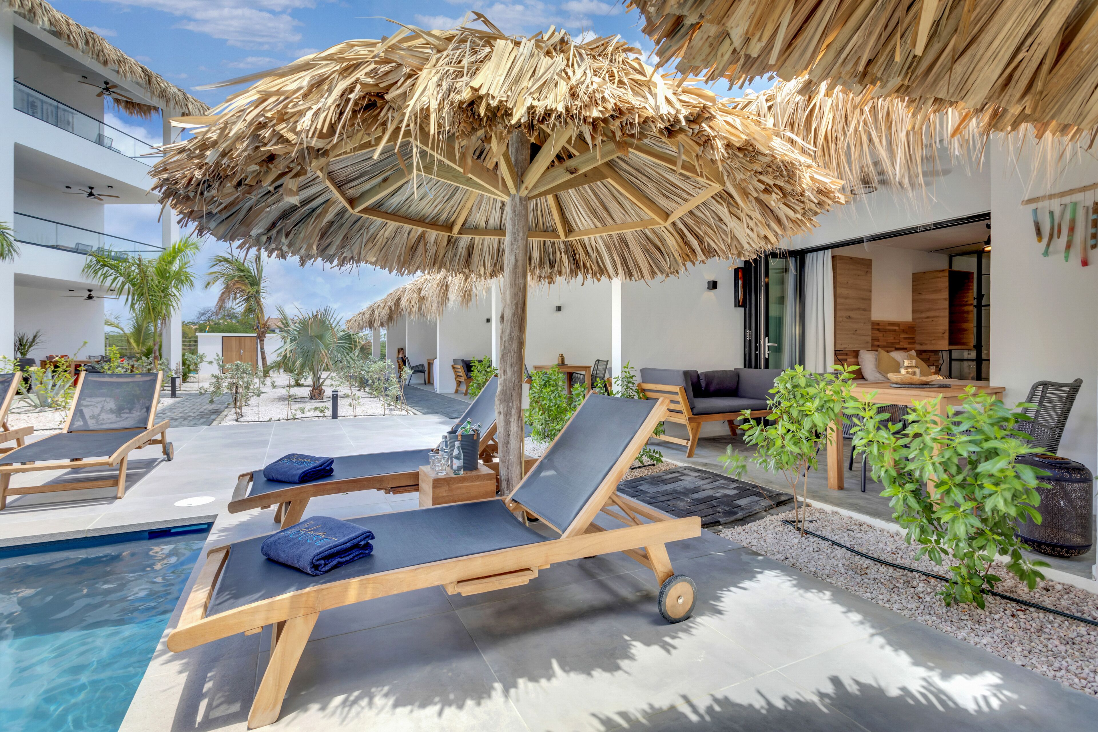 A poolside area with lounge chairs, a thatched umbrella, and a dining area with wooden furniture.