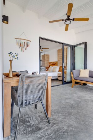 A modern room with a wooden dining table, a woven chair, a sofa, and a ceiling fan.