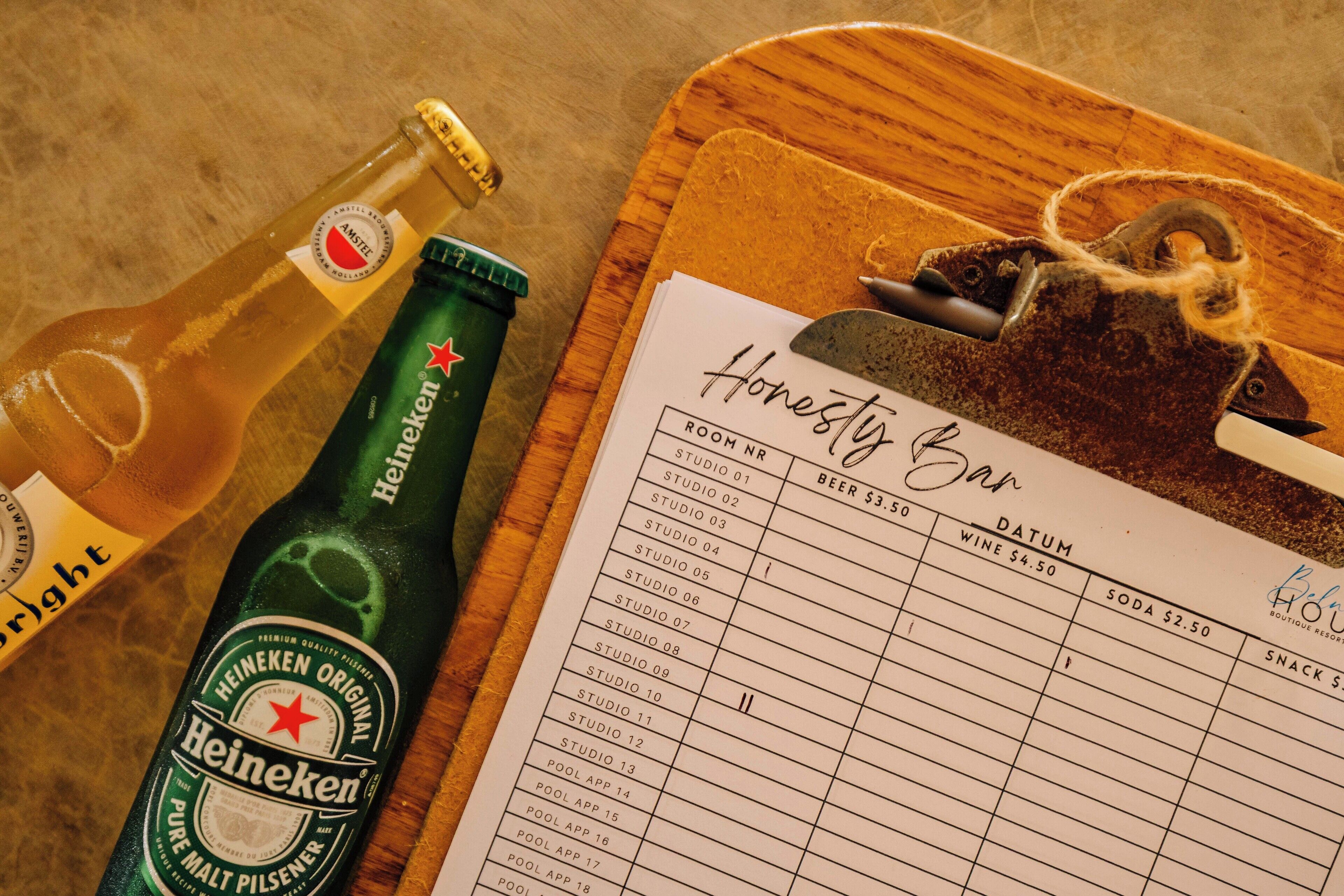 Een Heineken biertje en een klembord met een lijst van kamers bij Honesty Bar.