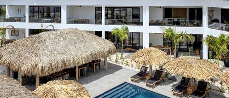 A modern hotel with a pool area, thatched umbrellas, and lounge chairs.