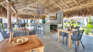 An outdoor dining area with thatched roof, wooden tables, and wicker chairs. - Belnem House Bonaire (Kralendijk)