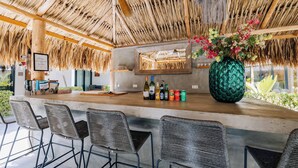 A bar area with a thatched roof, a large green vase with flowers, and a selection of bottles on the counter. - Belnem House Bonaire (Kralendijk)