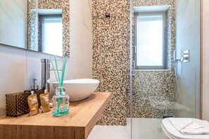 A modern bathroom with a wooden vanity, a white sink, a glass bottle, and a shower area with mosaic tiles.