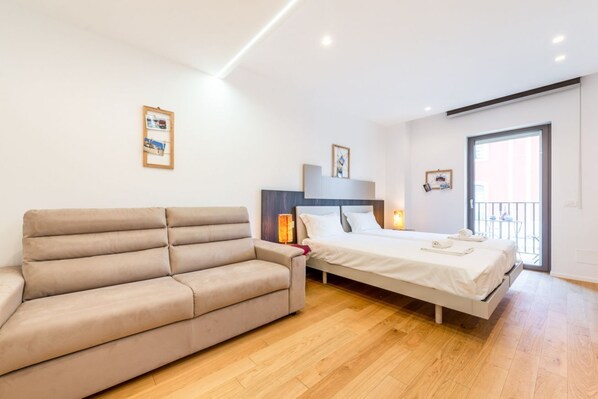 A modern bedroom with a sofa, a bed, a nightstand, and a window with a view.