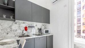 Een moderne keuken met grijze kastjes, een marmeren aanrecht, een magnetron en een rode waterkoker.