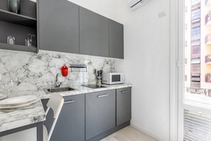 A modern kitchen with grey cabinets, a marble countertop, a microwave, and a red kettle.