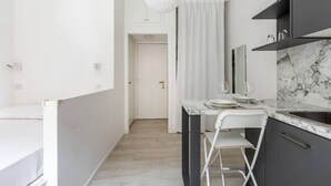 Een kleine keuken met een marmeren aanrecht, een witte stoel en een witte hanglamp.