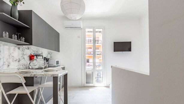 Een moderne keuken met marmeren aanrecht, een eethoek met een witte stoel, en een aan de muur bevestigde televisie.