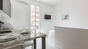 Een moderne keuken met een marmeren aanrecht, een eethoek met stoelen, een aan de muur bevestigde televisie en een balkon met uitzicht op gebouwen.
