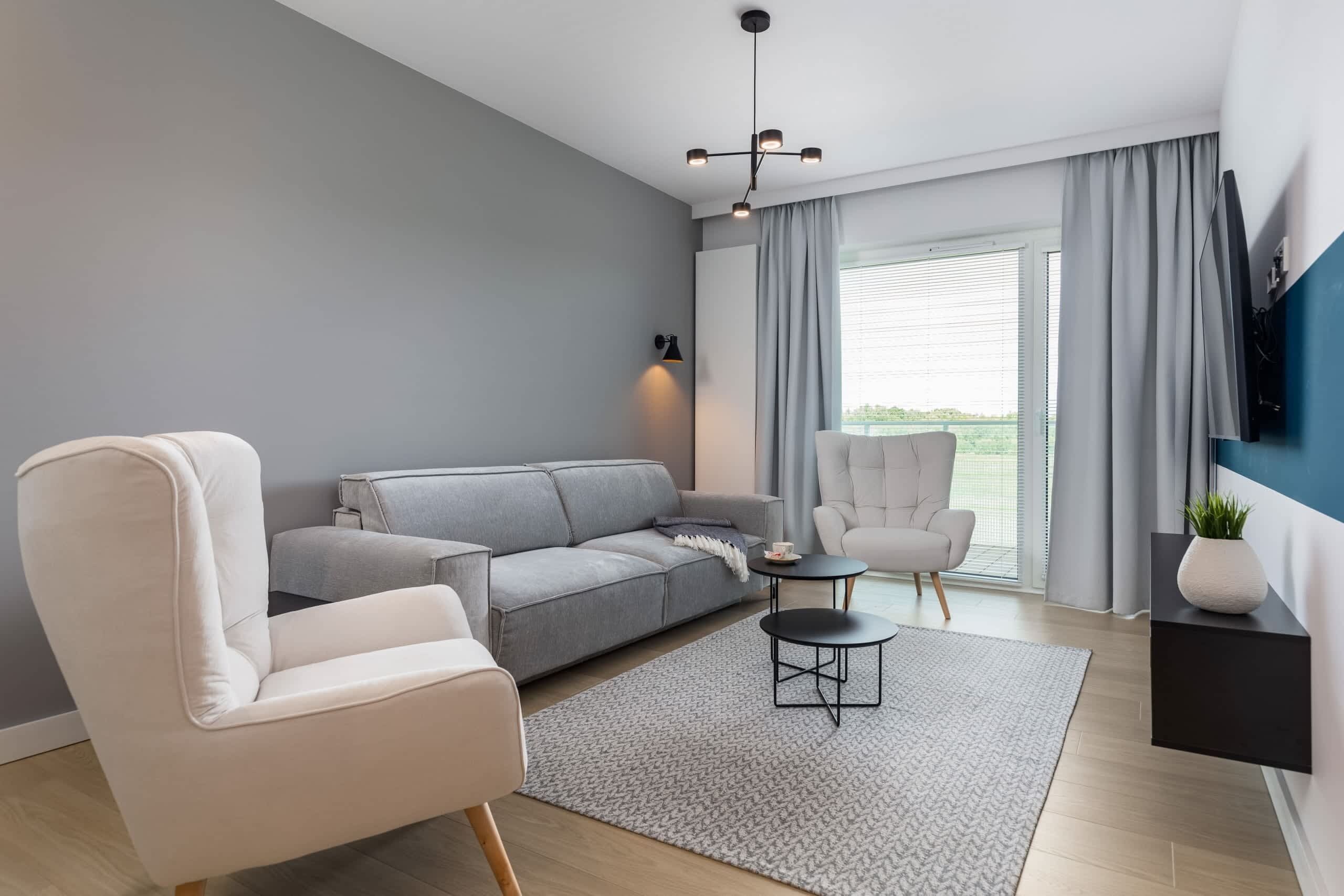 Ein modernes Wohnzimmer mit einem grauen Sofa, einem weißen Sessel, einem kleinen runden Tisch und einem an der Wand befestigten Fernseher.