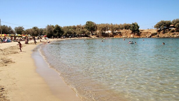 Une plage avec une eau claire et peu profonde, des gens qui se baignent et des parasols sur le sable.