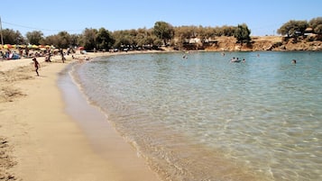 Ein Strand mit klarem, flachem Wasser, Menschen beim Schwimmen und Sonnenschirmen im Sand.