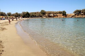 A beach with clear shallow waters, people swimming, and umbrellas on the sand.