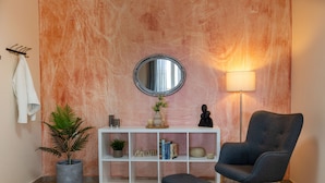 Un salon moderne avec une console blanche, un miroir rond, un fauteuil foncé, une lampe sur pied et une plante en pot.