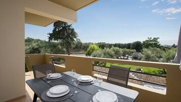 Ein Balkon mit Esstisch, der auf einen Garten und entfernte Gebäude blickt.