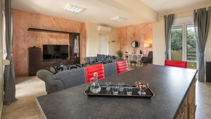 Un salon moderne avec une grande table basse noire, des canapés gris et rouges, un téléviseur à écran plat et un coin repas comprenant une longue table et des chaises.