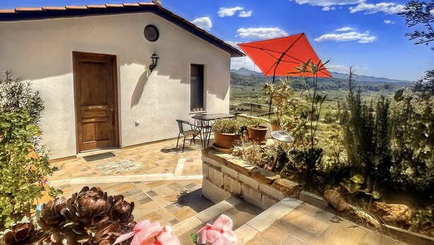 Una casa con un patio, un ombrello rosso e fiori rosa in primo piano.