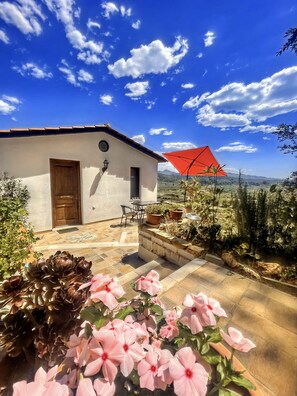 Ein Haus mit Terrasse, einem roten Sonnenschirm und rosa Blumen im Vordergrund.