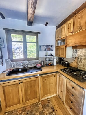 Une cuisine avec des meubles en bois, une cuisinière à gaz, un évier et une fenêtre donnant sur un paysage verdoyant.