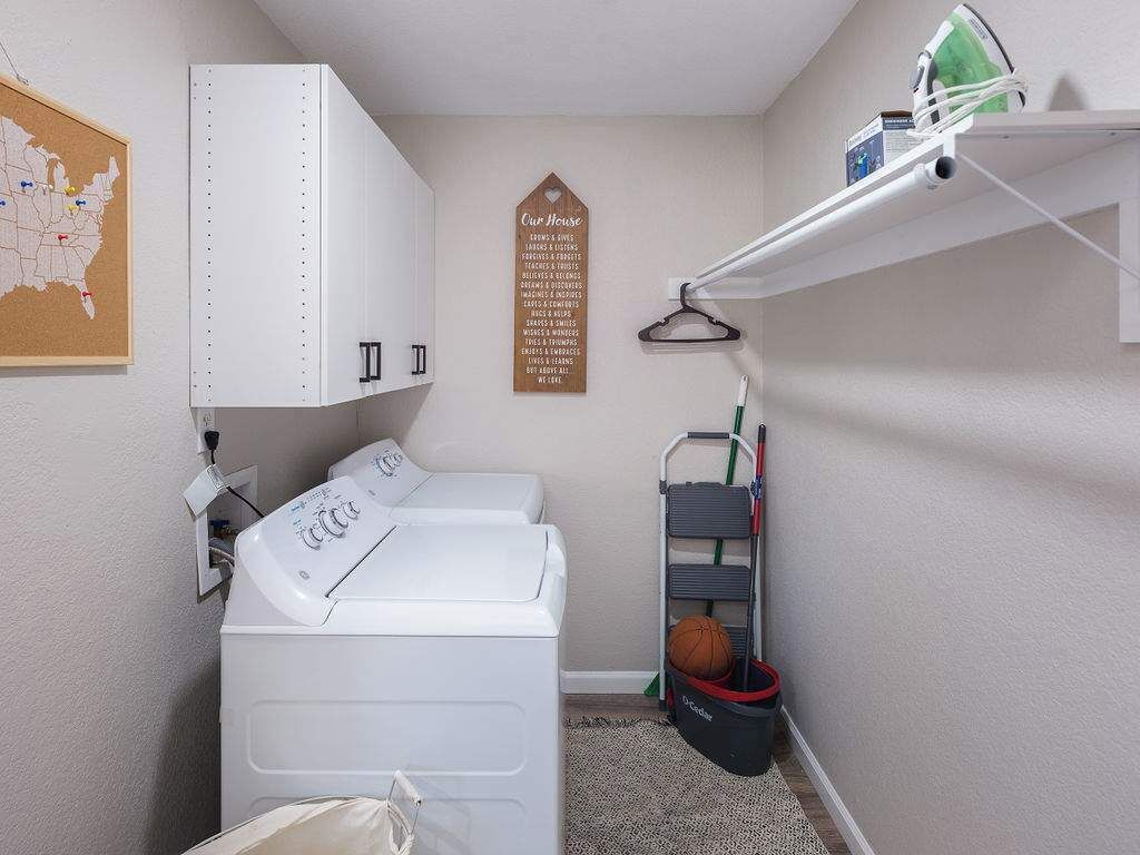 A laundry room with a washing machine, dryer, ironing board, and a map on the wall.