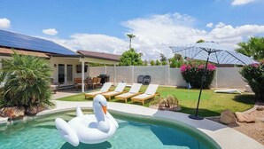 Piscina com um flutuador de cisne, cadeiras de descanso, um alpendre coberto e um painel solar.